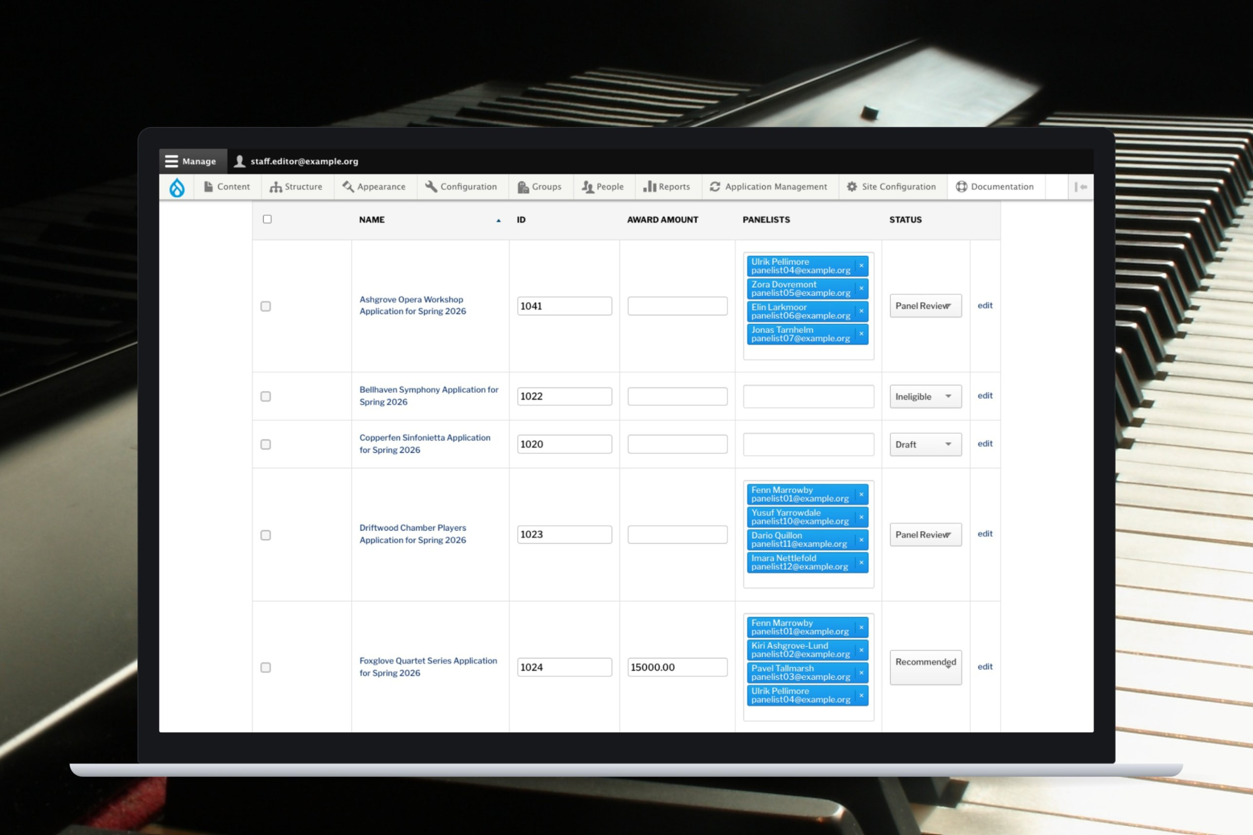 ApplyCycle editable application grid on a laptop, showing award amounts, panelist assignments, and statuses, over a photo of piano keys